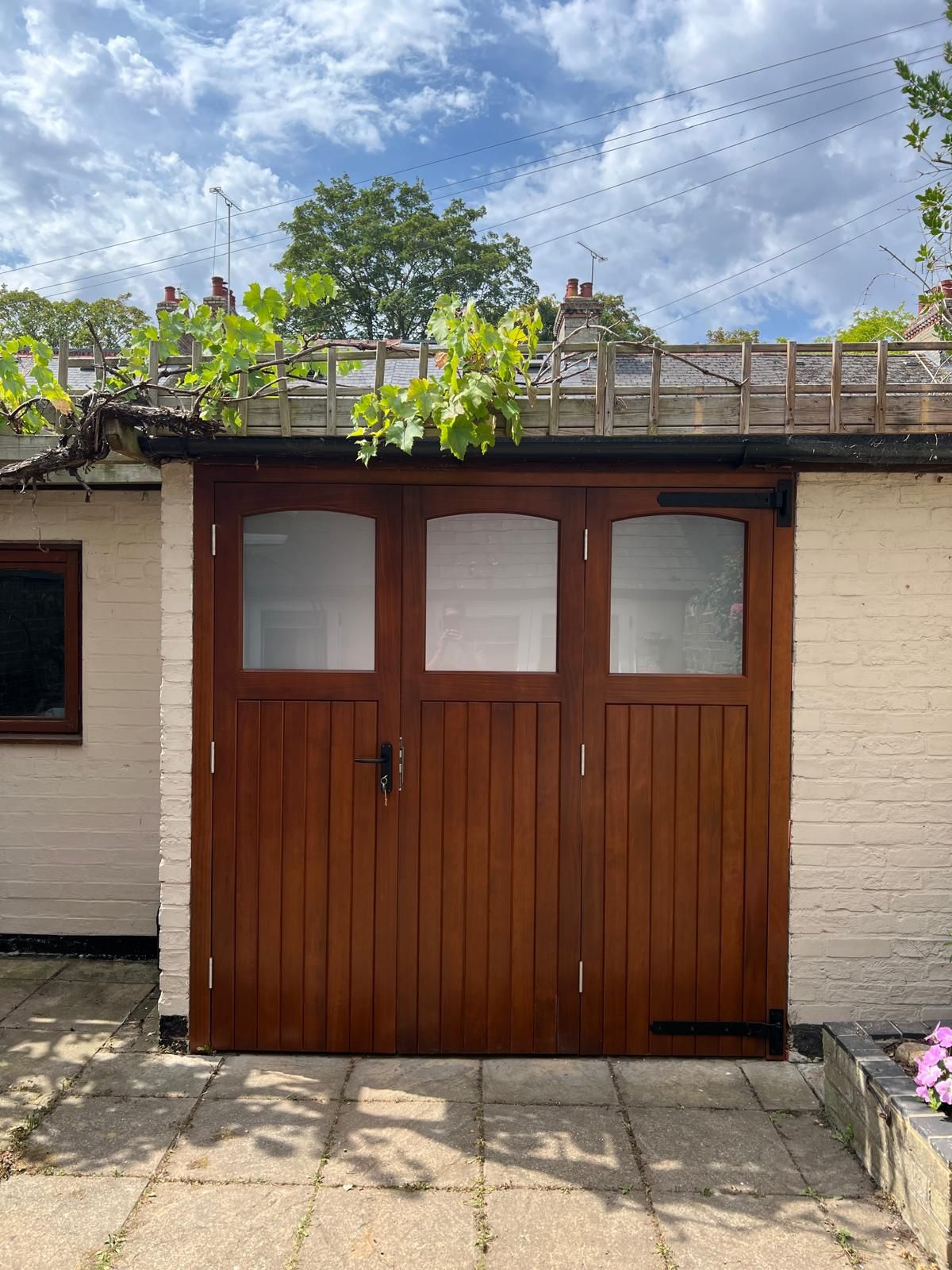 Accoya timber side-hinged garage doors with glazed upper panels on a brick outbuilding