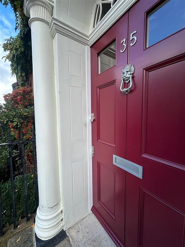 Close-up of burgundy entrance door showing lion door knocker and house number