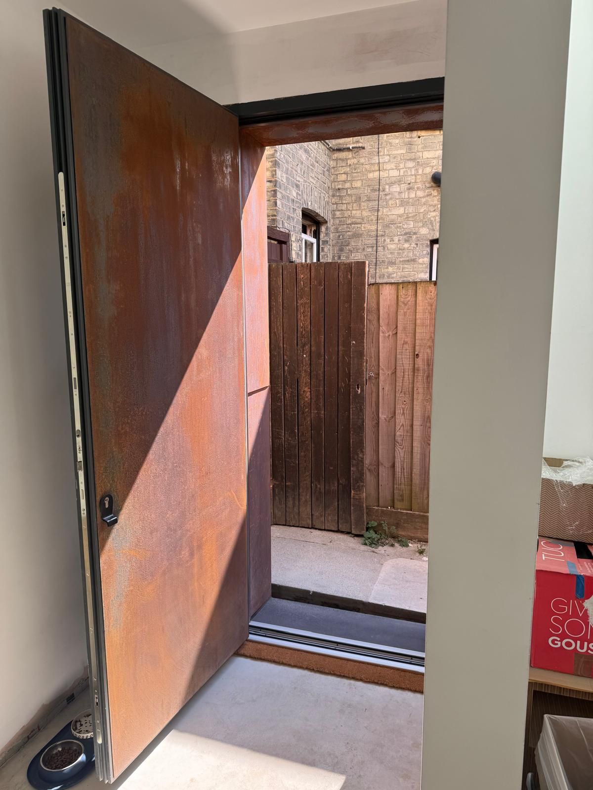 Contemporary corten steel-effect flush entrance door open to garden passage