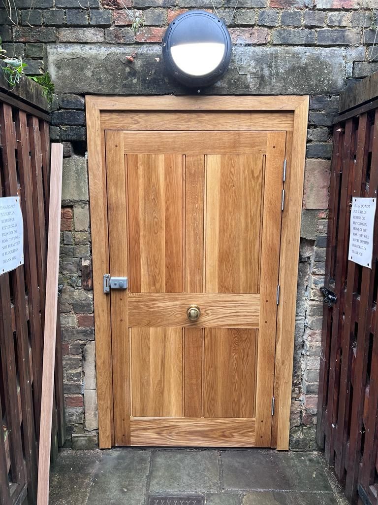 Bespoke oak flush panelled door with brass knob in rear brick alcove