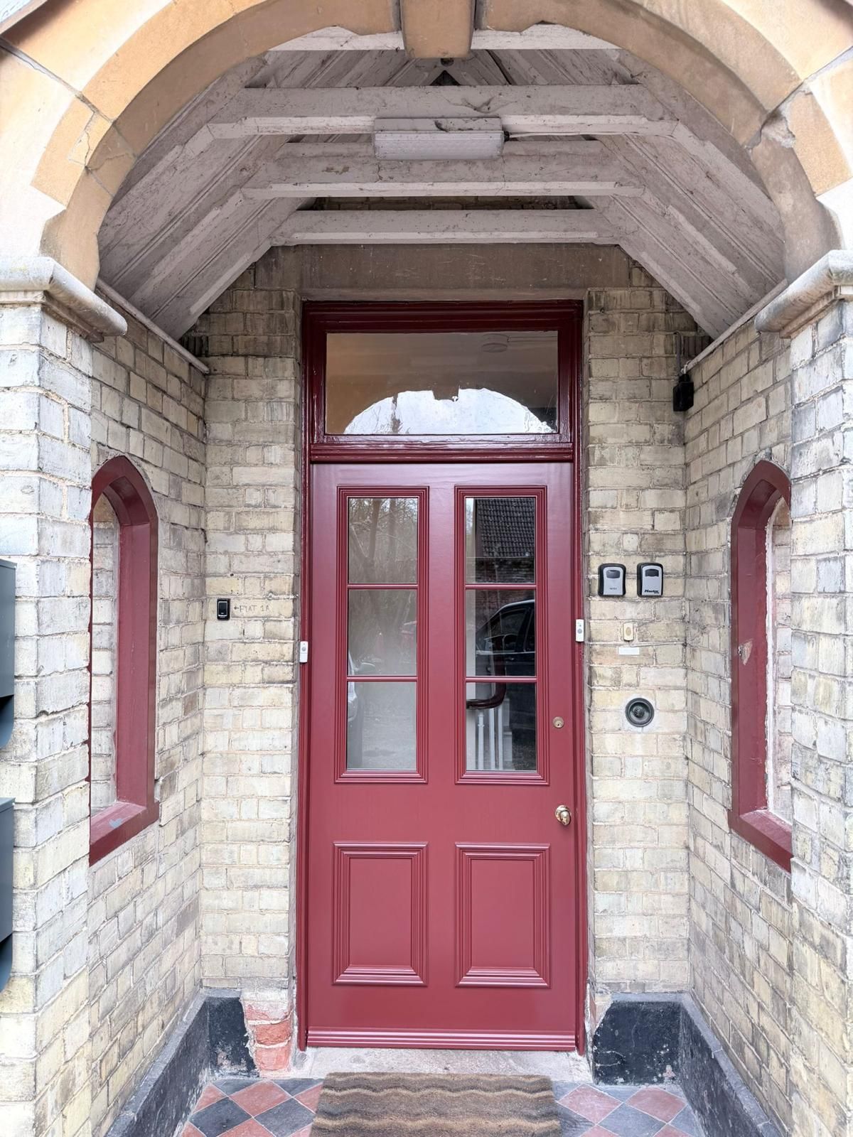 Red multi-pane glazed entrance door set within stone archway porch
