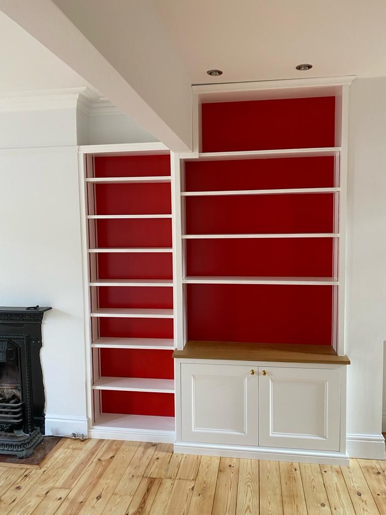 Fitted alcove bookshelves with red-painted backs above storage cupboard