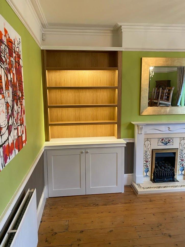 Fitted alcove shelving with lighting and cupboard beside a fireplace