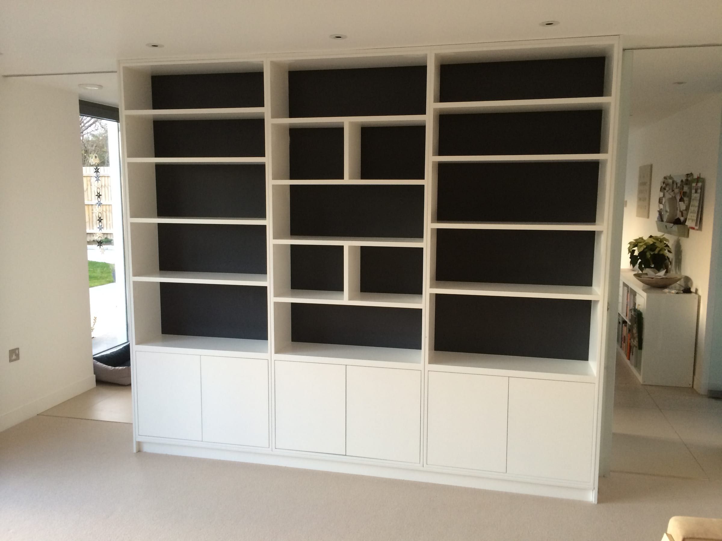 Full-wall fitted shelving and cupboard storage unit dividing a room