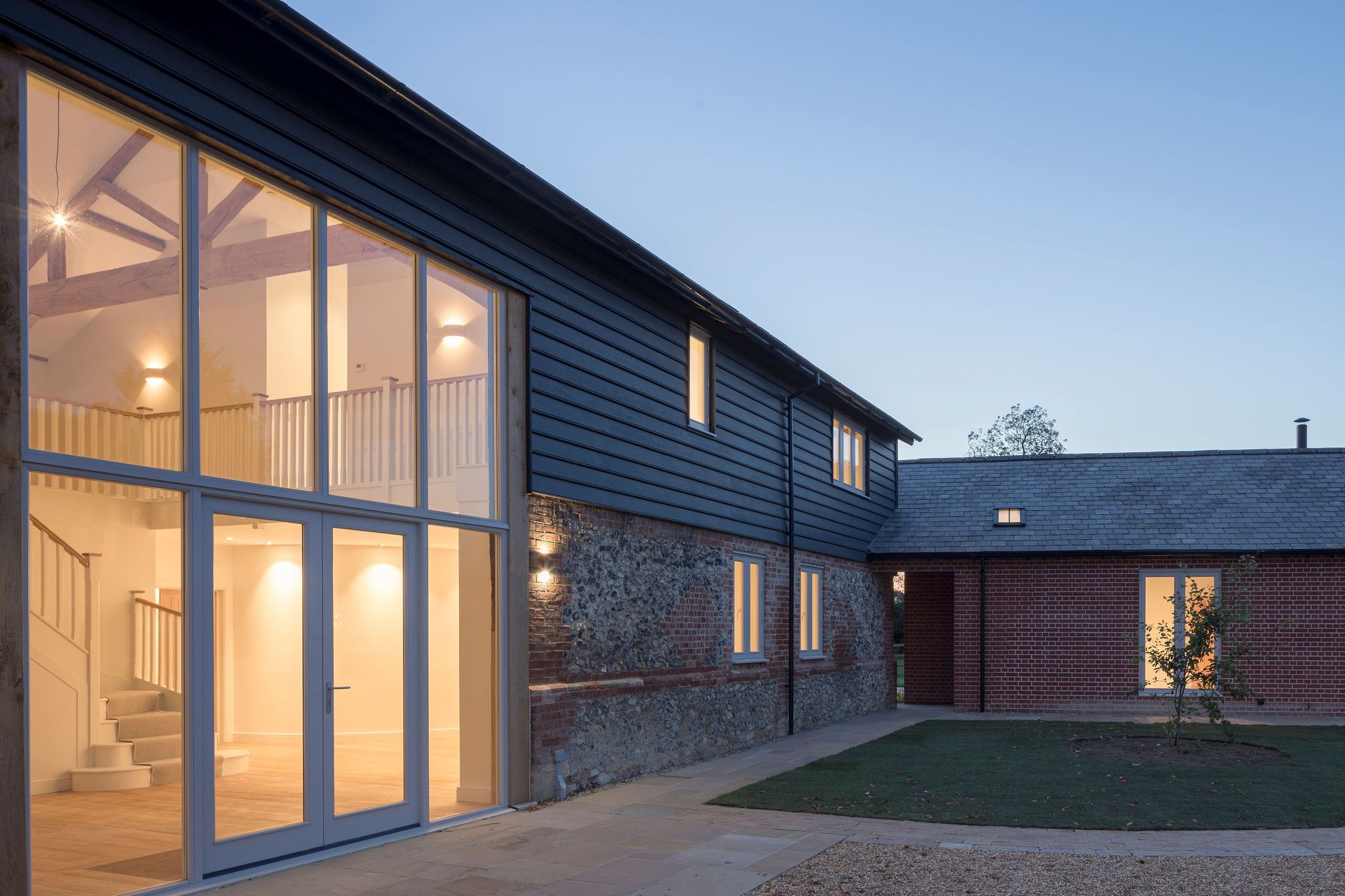 Full-height glazed timber gable entrance doors lit at dusk, oak trusses visible inside
