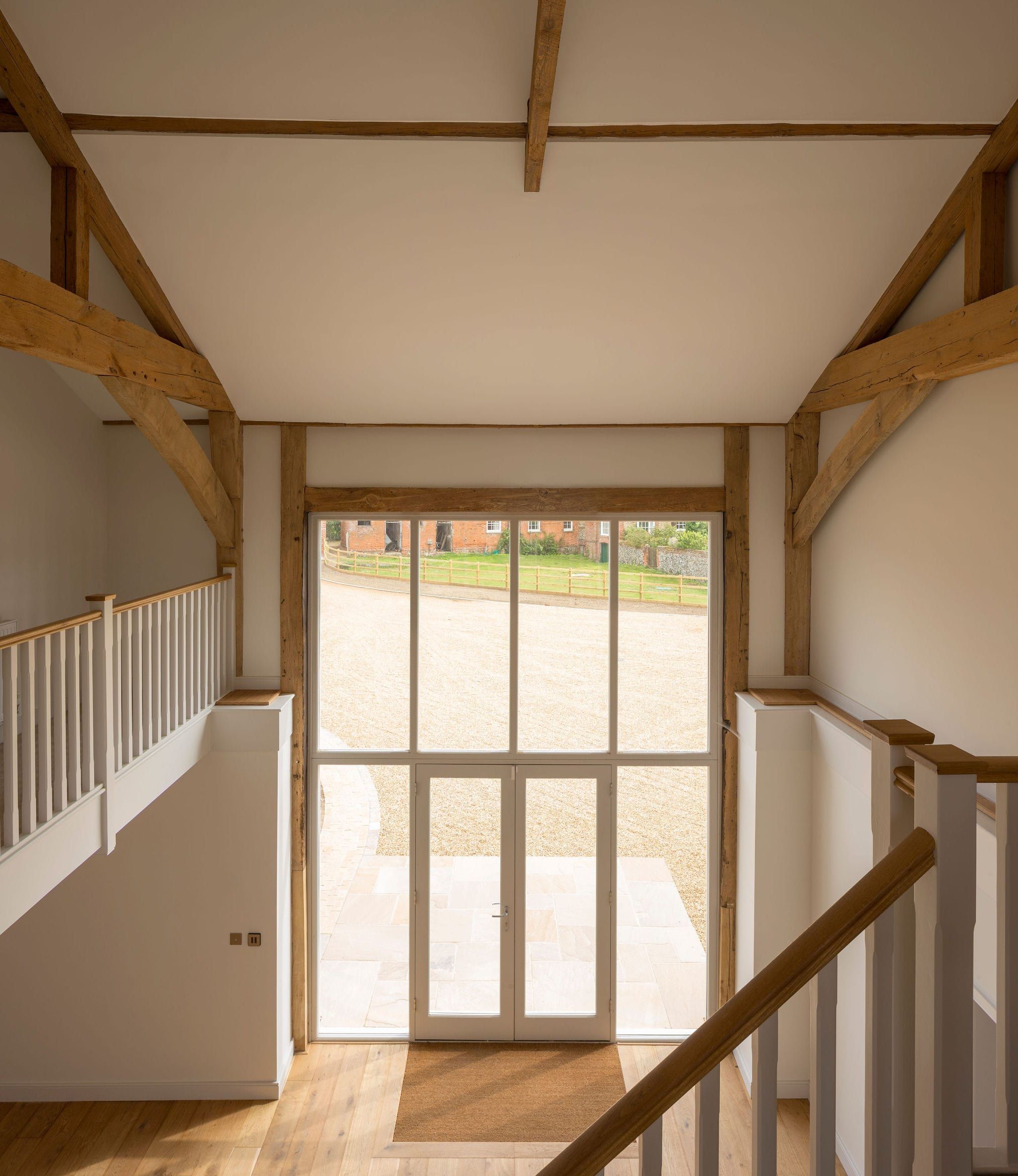 Interior landing view through tall timber glazed doors overlooking gravel driveway