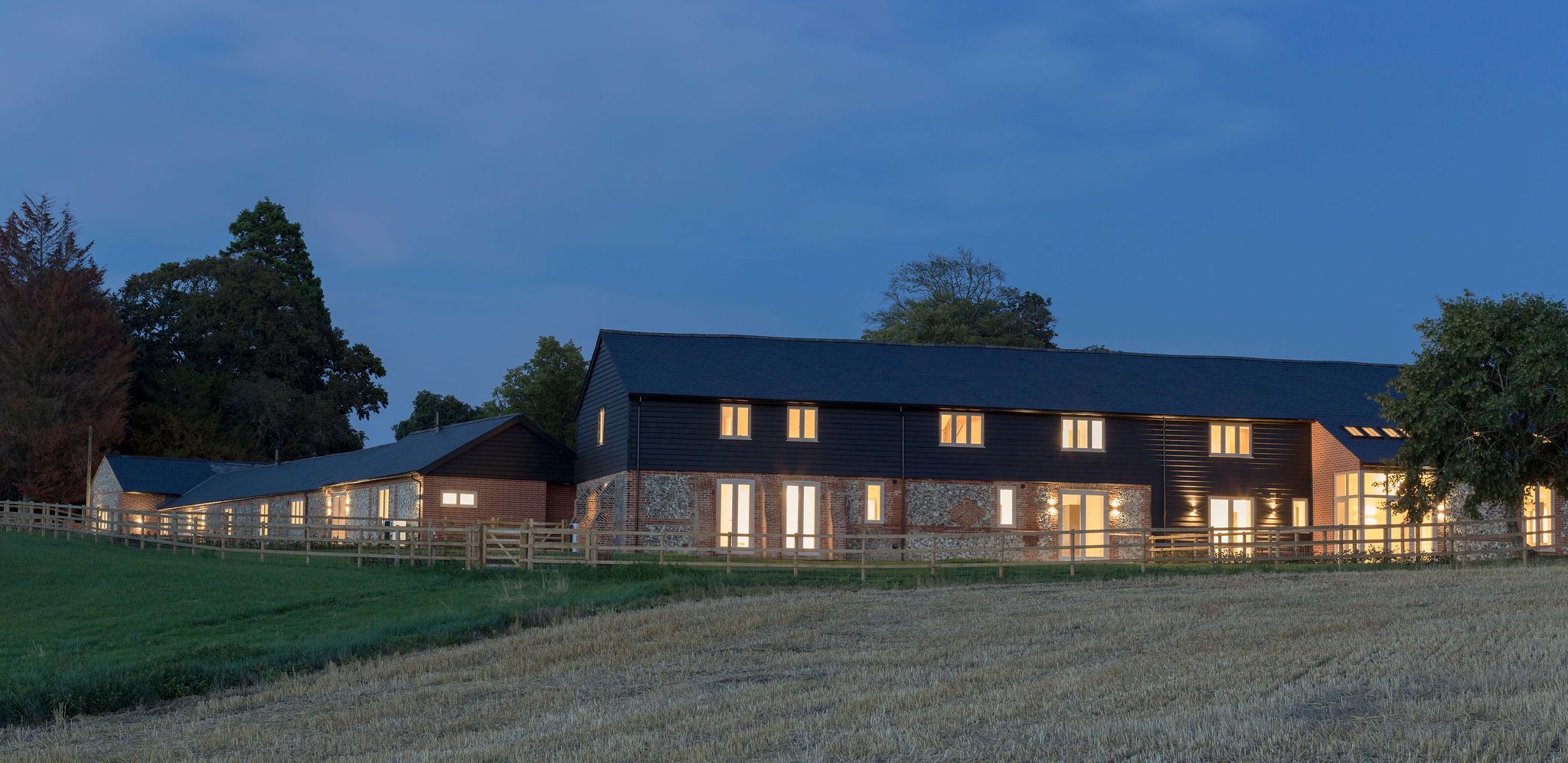 Converted barn complex at dusk with illuminated timber windows and doors