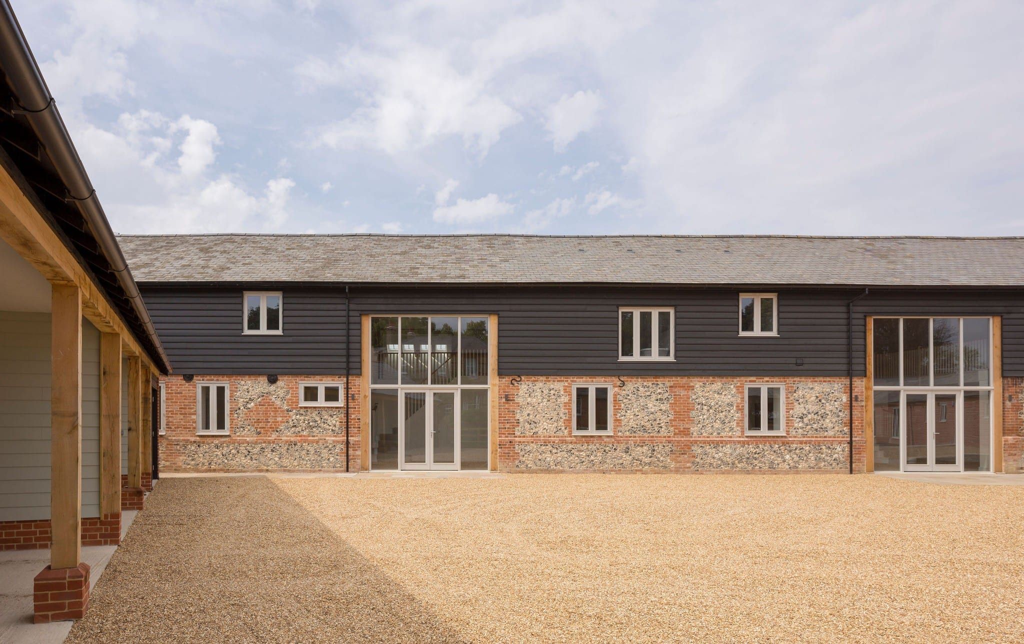 Converted barn with dark cladding, flint and brick walls, gravel courtyard