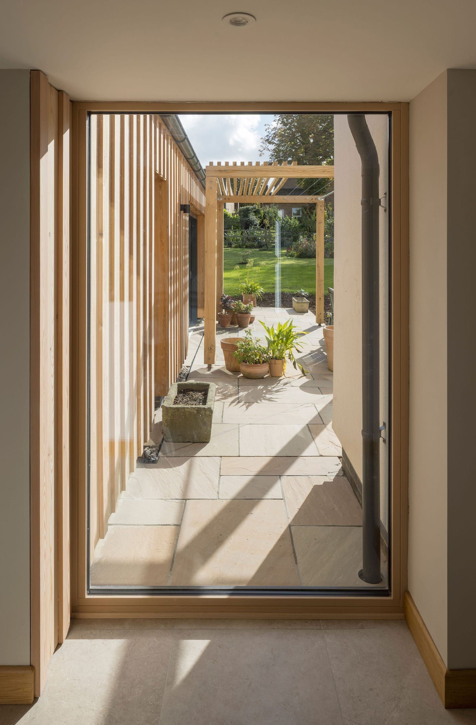 Glazed view along oak-slatted extension corridor to patio and pergola