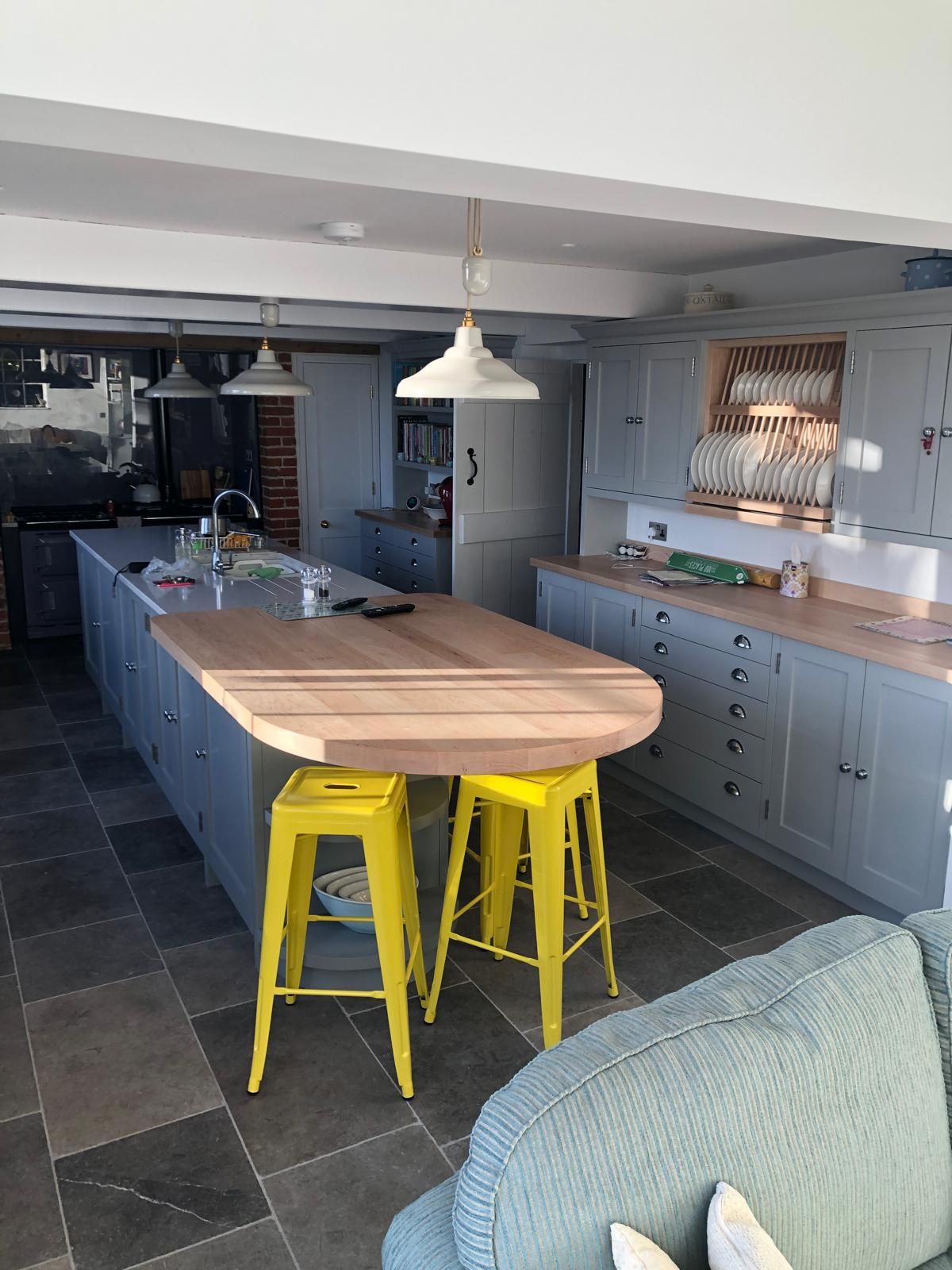 Grey shaker kitchen island with oval oak breakfast bar, yellow stools and oak plate rack cabinet