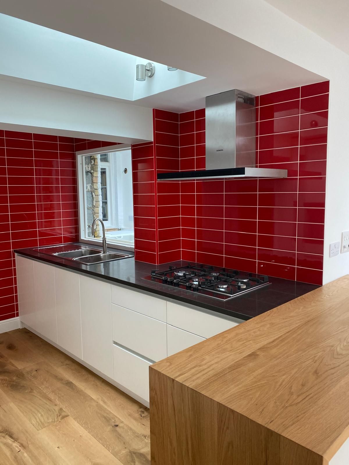 White kitchen island with black worktop, inset sink and glossy red brick-tile splashback