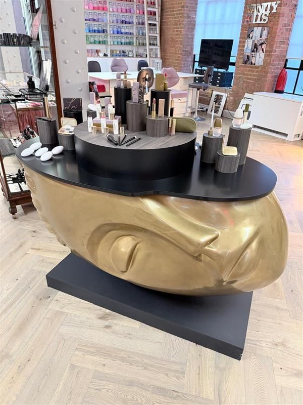 Bespoke tabletop with sculptural gold face base displaying makeup products