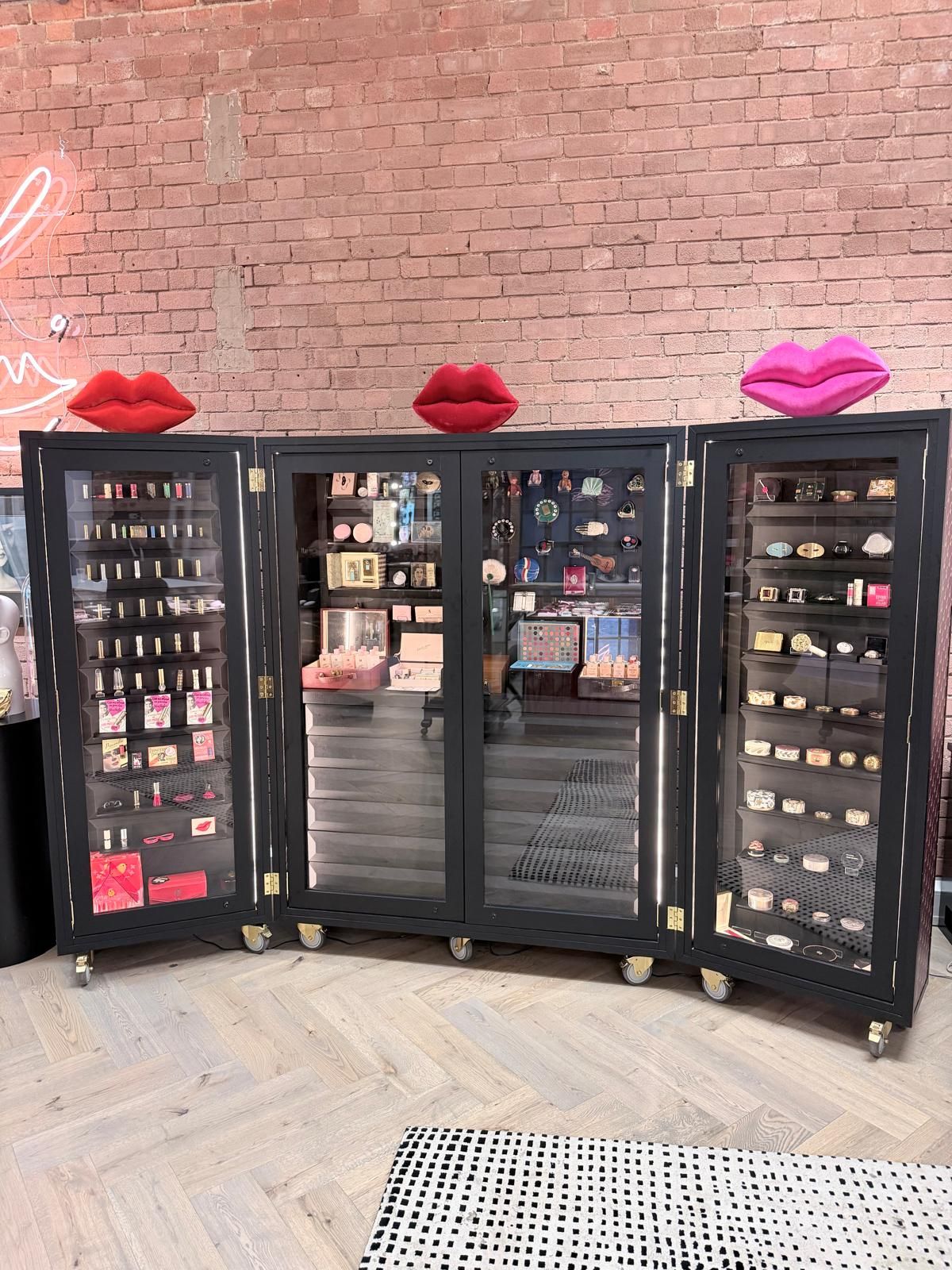 Bespoke makeup trunk open, glazed shelves of cosmetics, pink lip sculptures on top