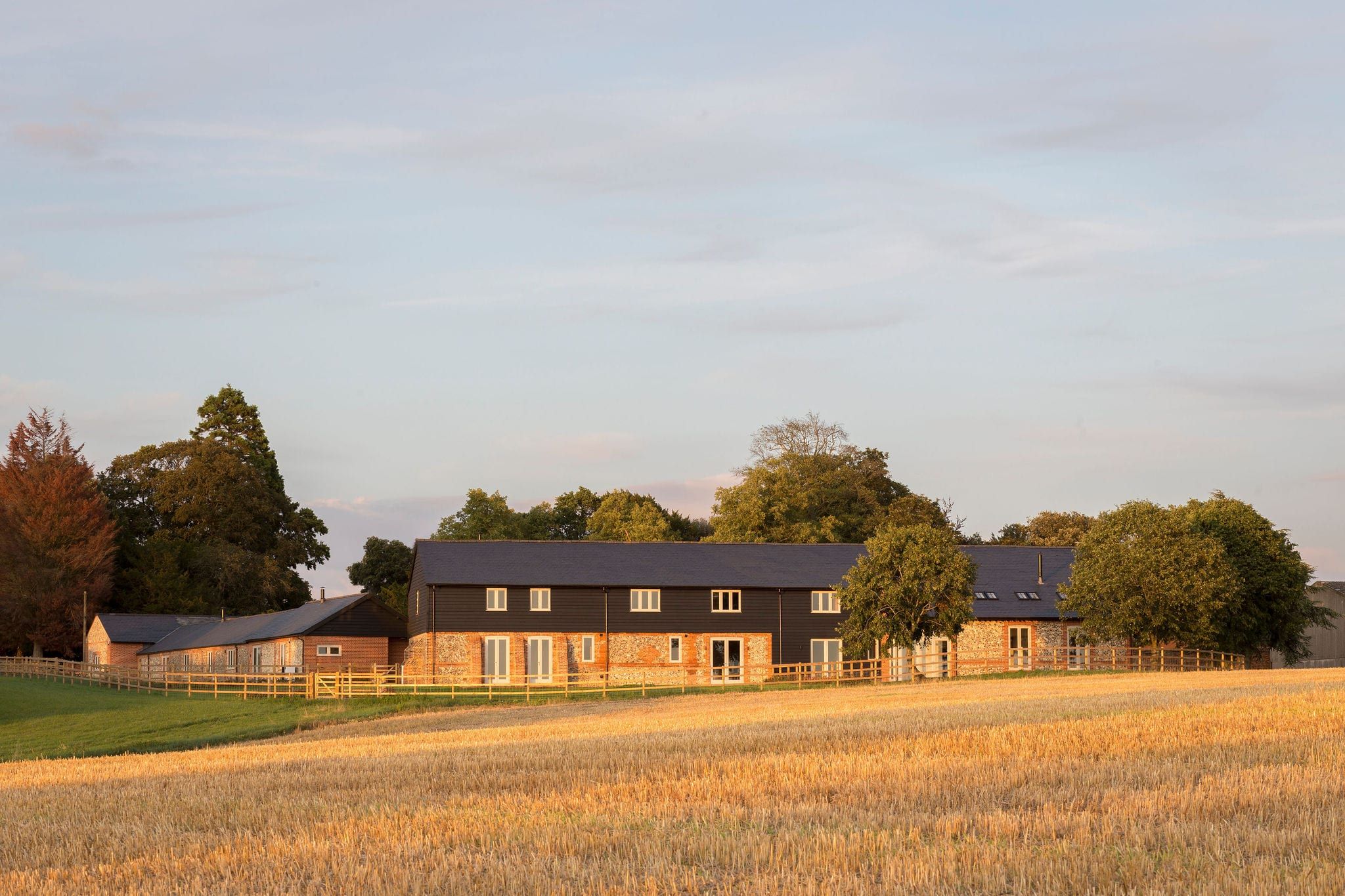 Converted barn buildings seen across a harvested field at dusk