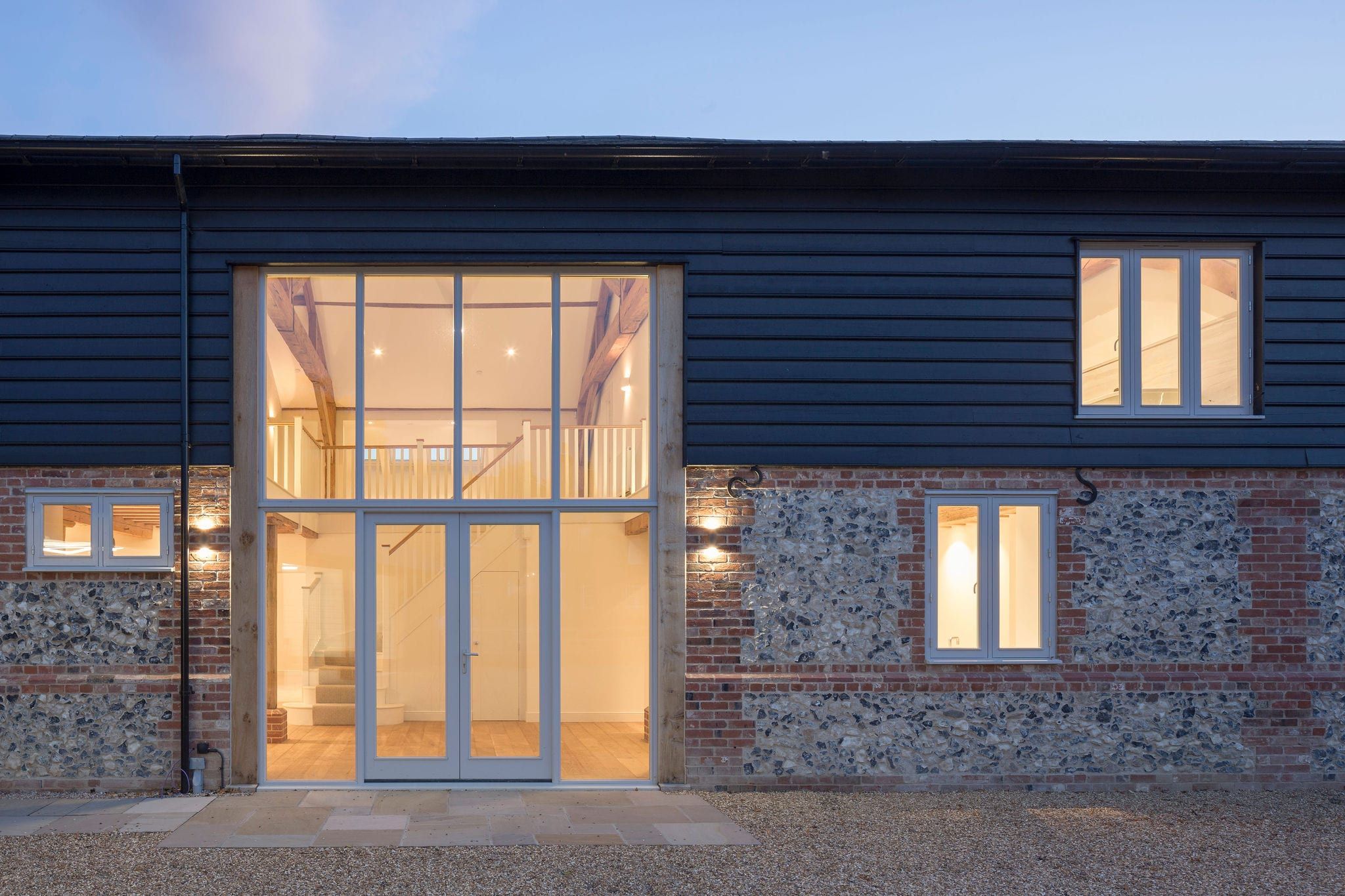 Timber-clad barn conversion with glazed entrance and staircase at dusk