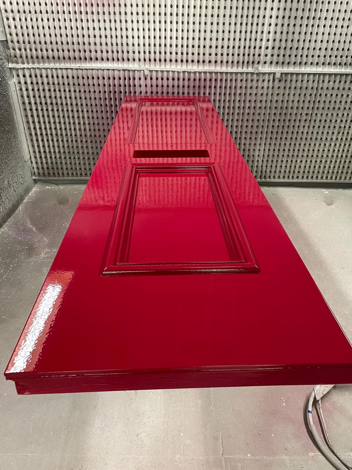 Glossy red-sprayed panelled door on a trolley inside the spray booth