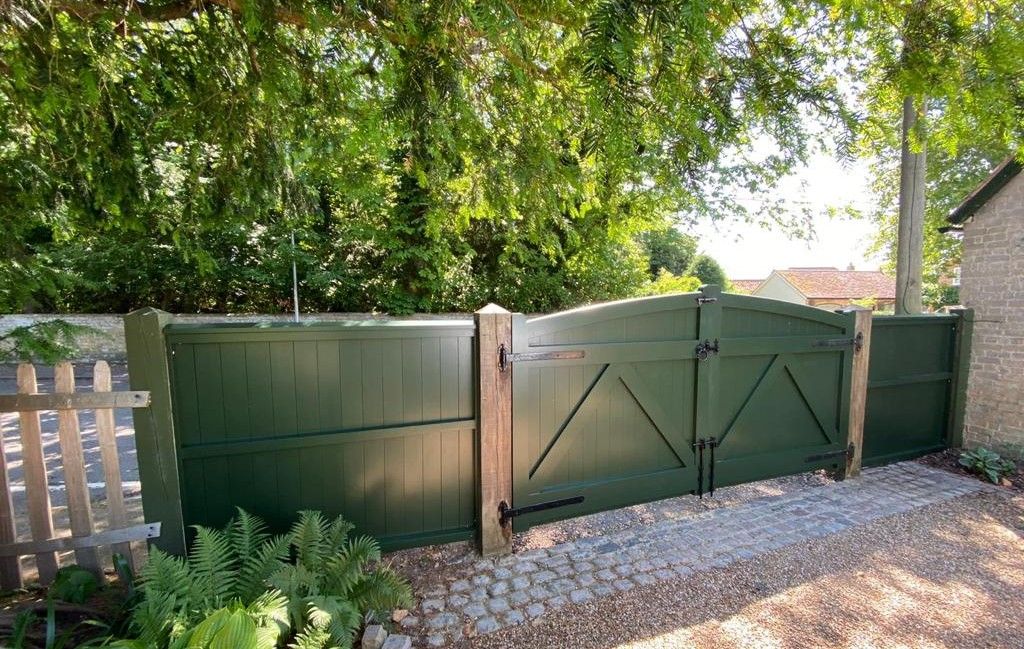 Sage green spray-painted timber driveway gates set in a brick wall