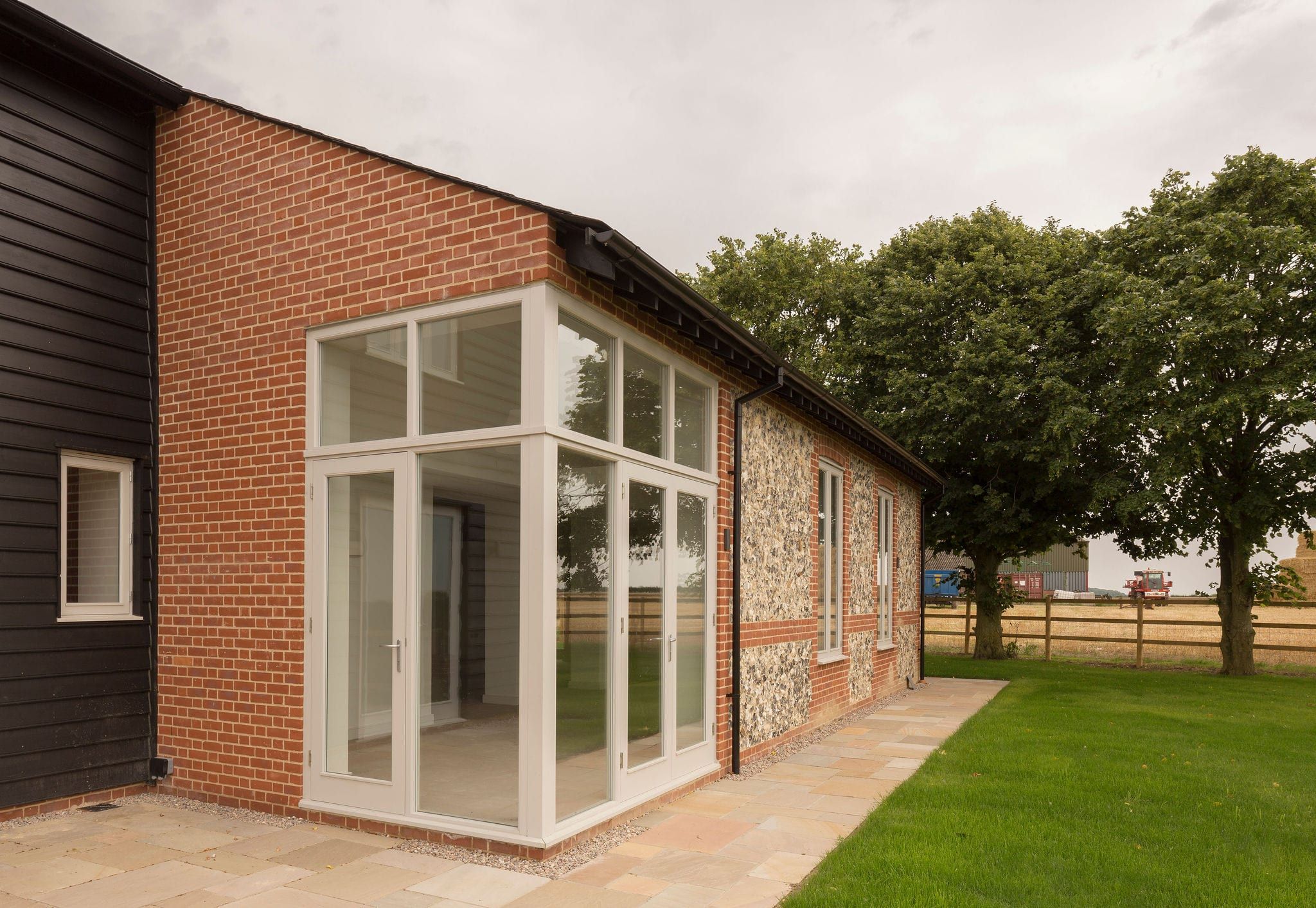 Painted timber French doors in glazed gable extension on brick and flint barn