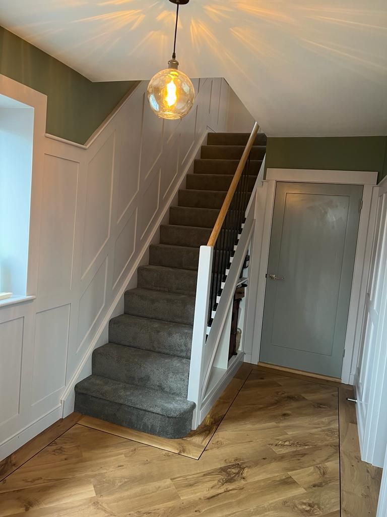 Carpeted staircase with white panelled walls and wooden handrail