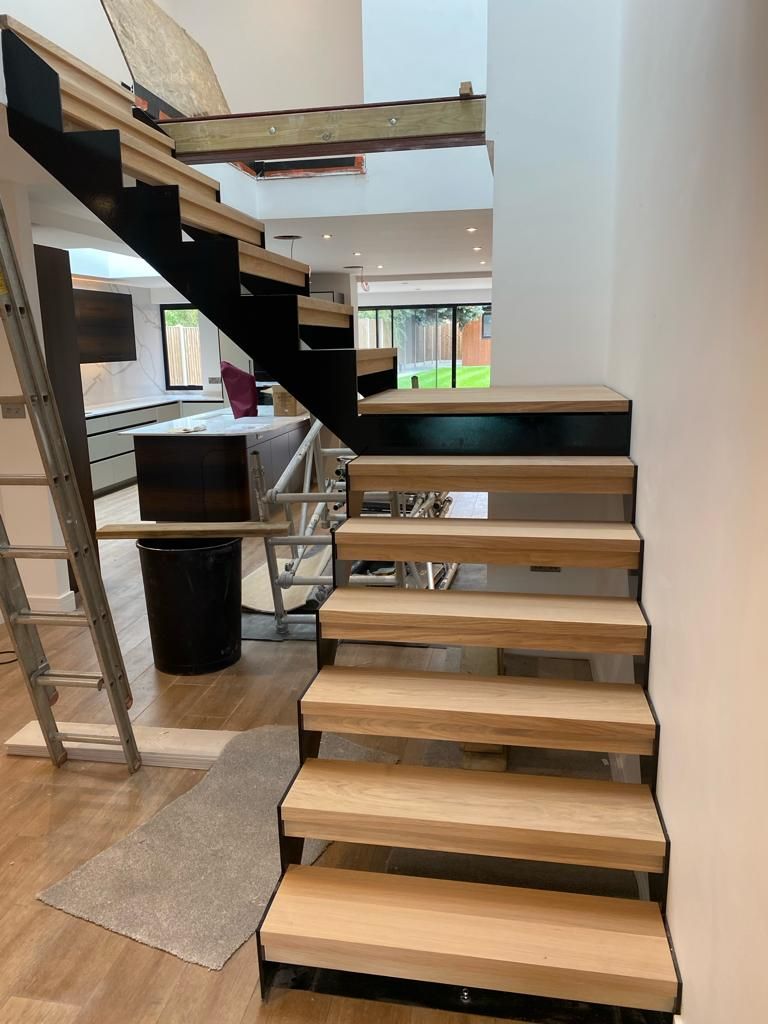 Modern cantilevered oak stair treads on black steel frame, under construction