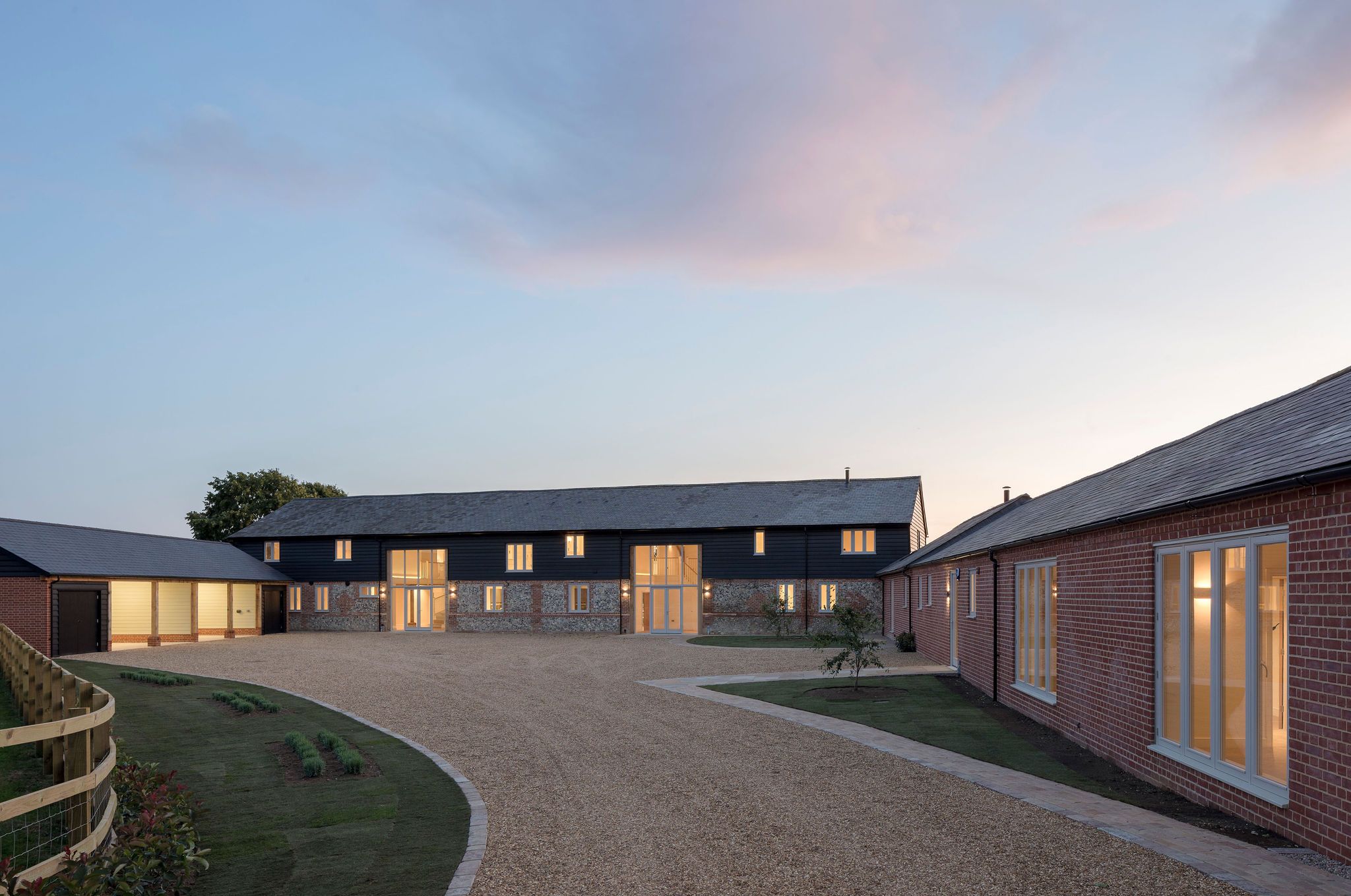 Converted flint and brick barn at dusk with illuminated timber casement windows