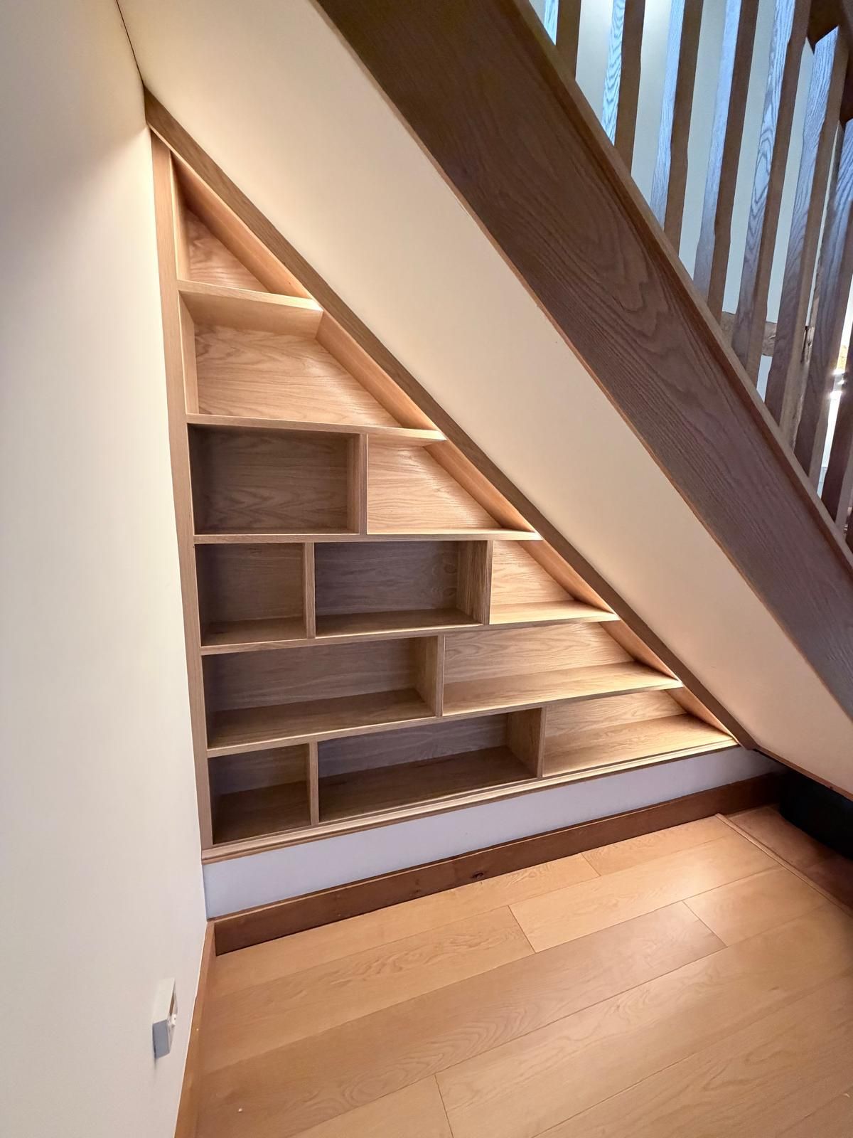 Triangular oak understairs shelving unit beneath staircase, angled view