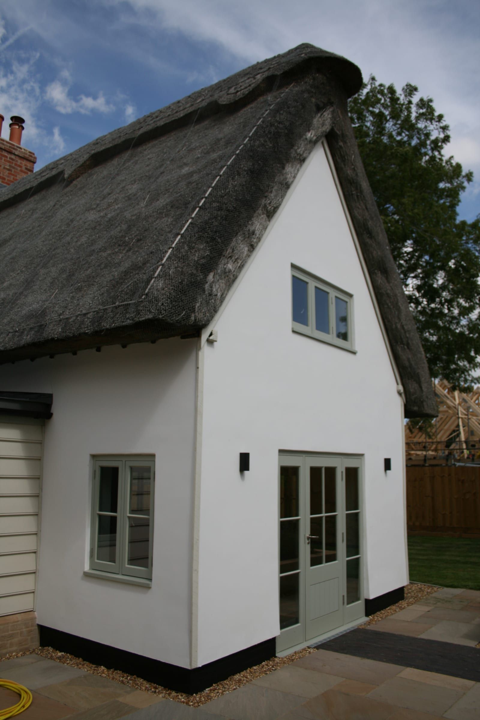Thatched cottage extension with sage-green vacuum glass windows and French doors
