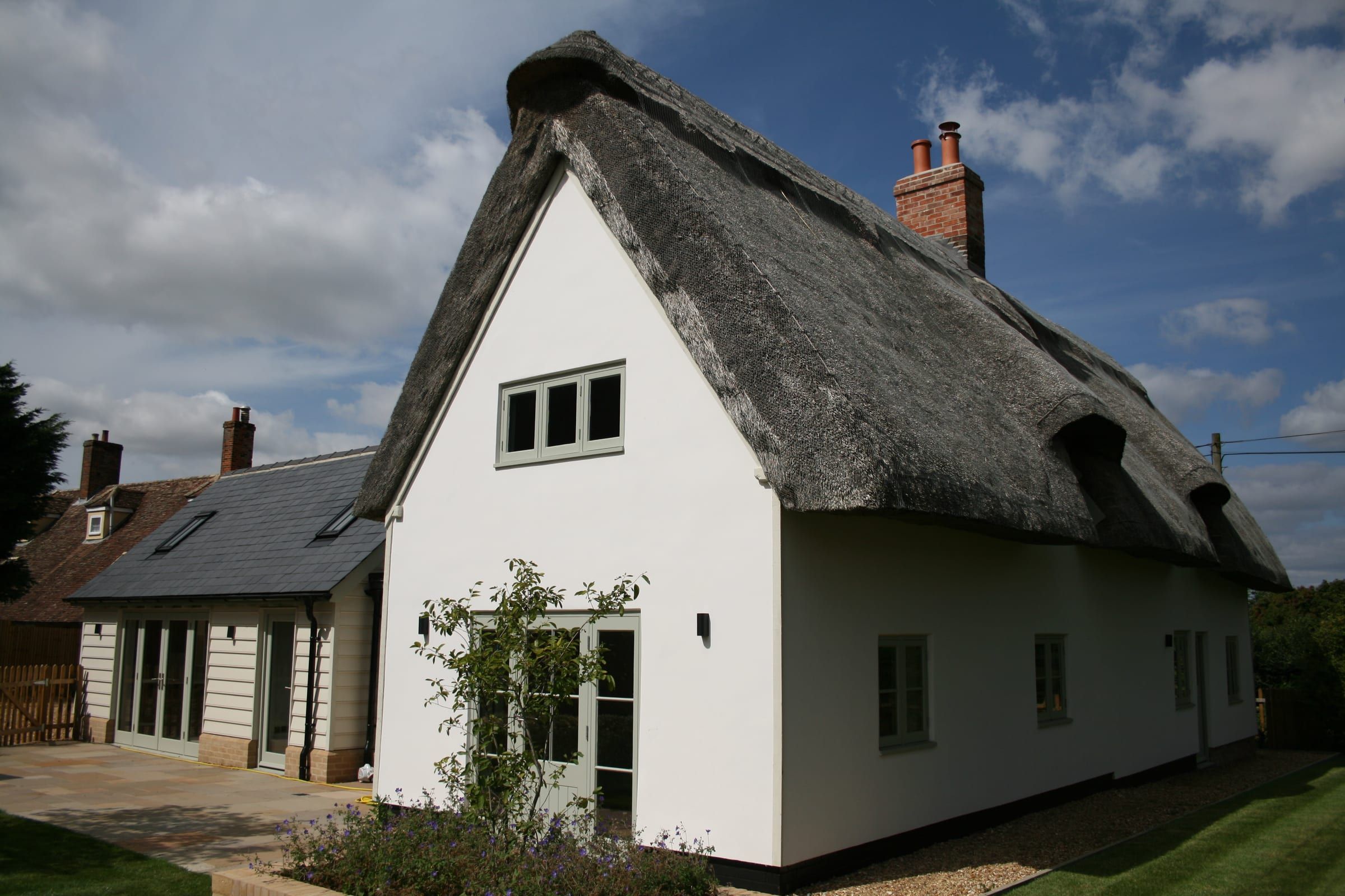 Thatched cottage gable end with sage-green vacuum glass windows and doors