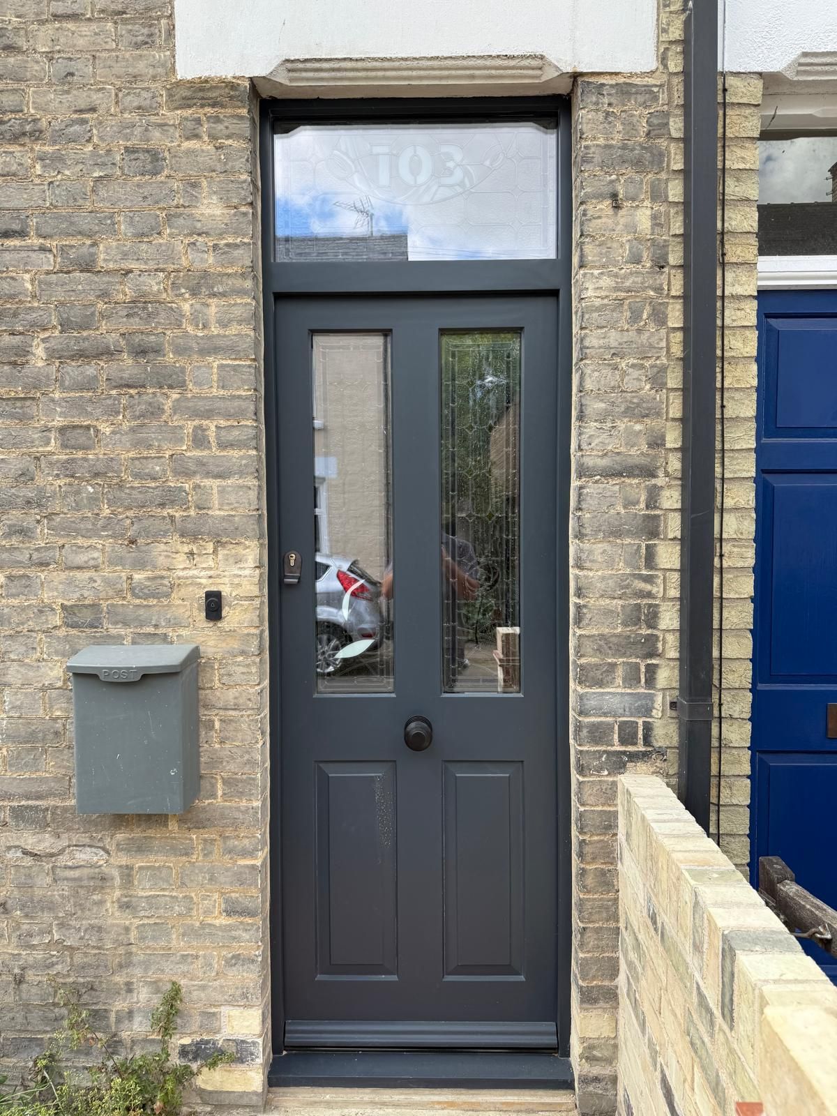 Exterior navy entrance door with leaded glass fanlight showing house number 103